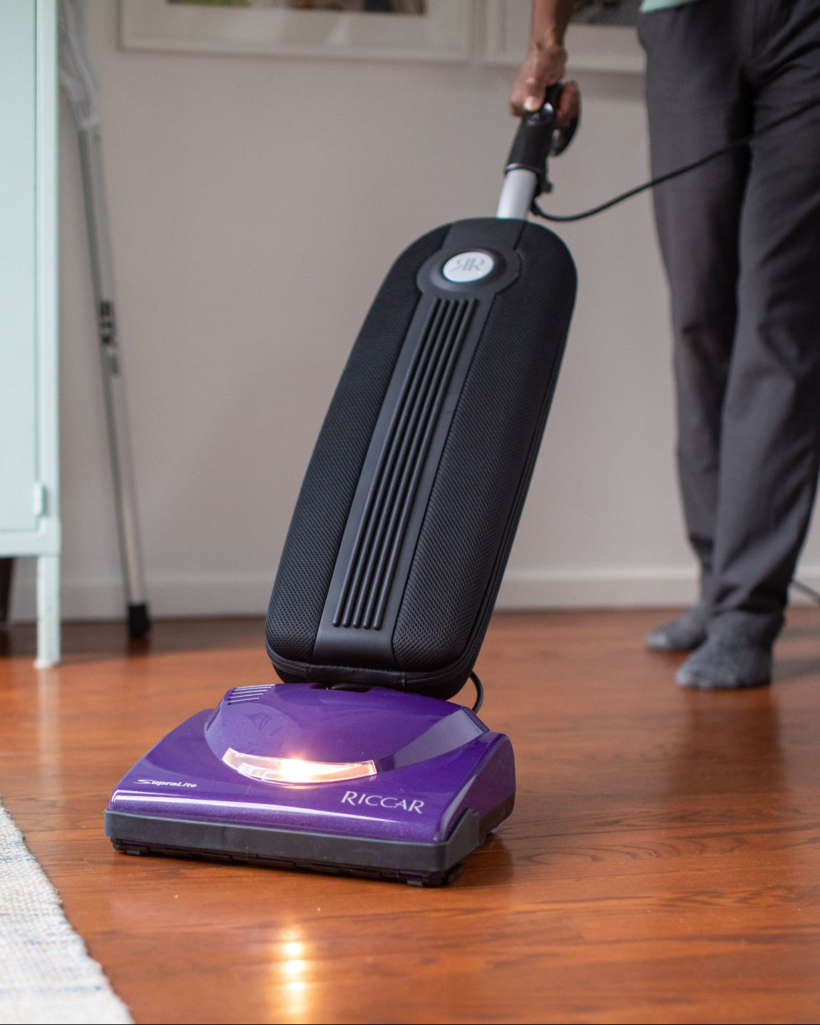 Person using a purple and black vacuum cleaner on a wooden floor transitioning to a rug.