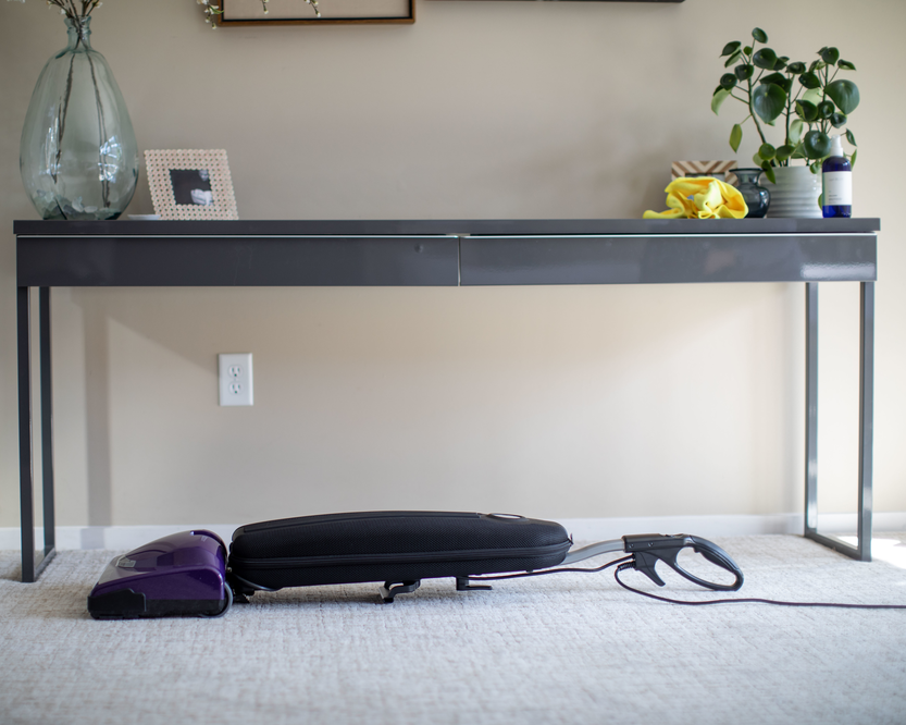 Vacuum cleaner on the floor in front of a table with decorative items.