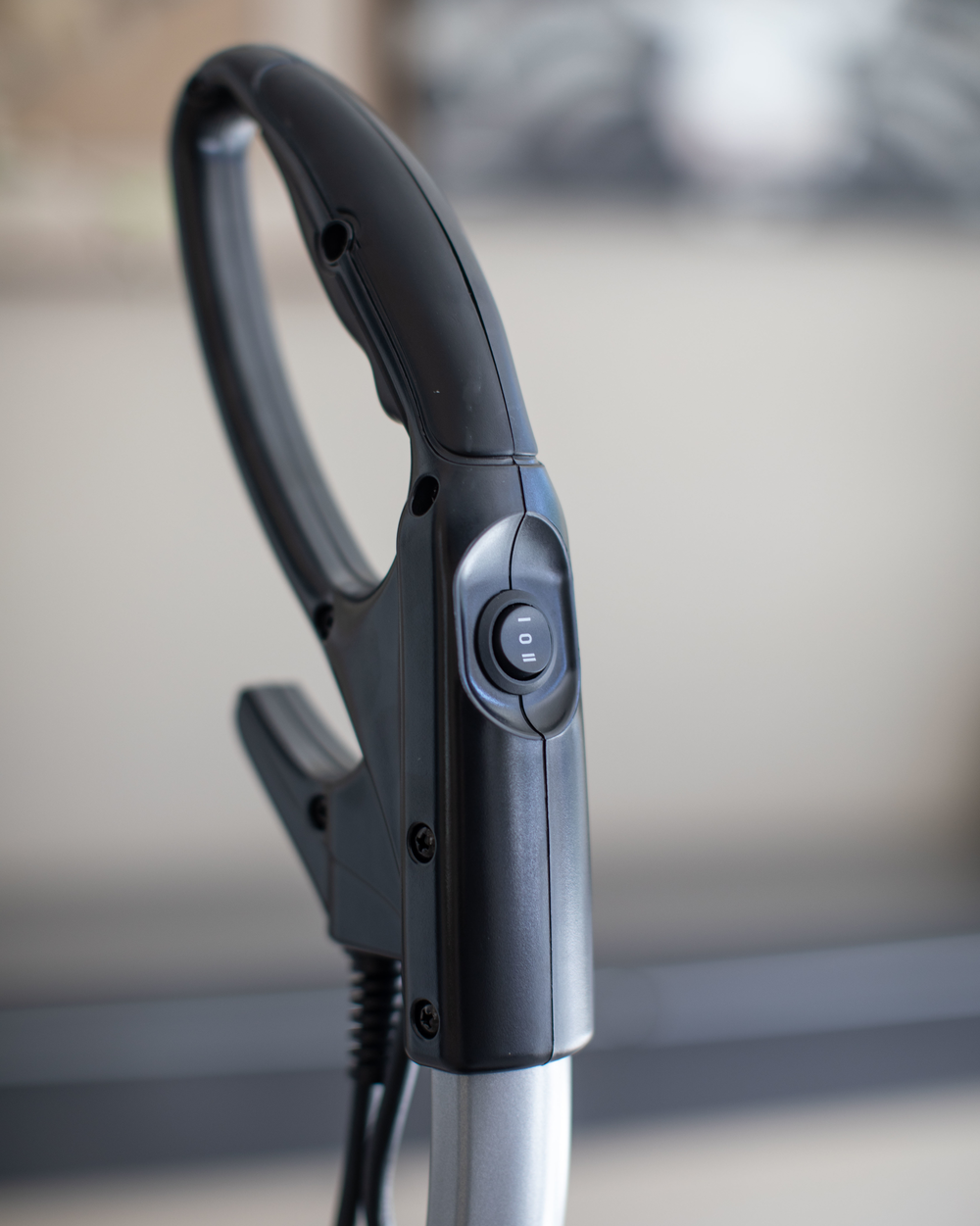 Close-up of a black and silver vacuum cleaner handle with blurred background