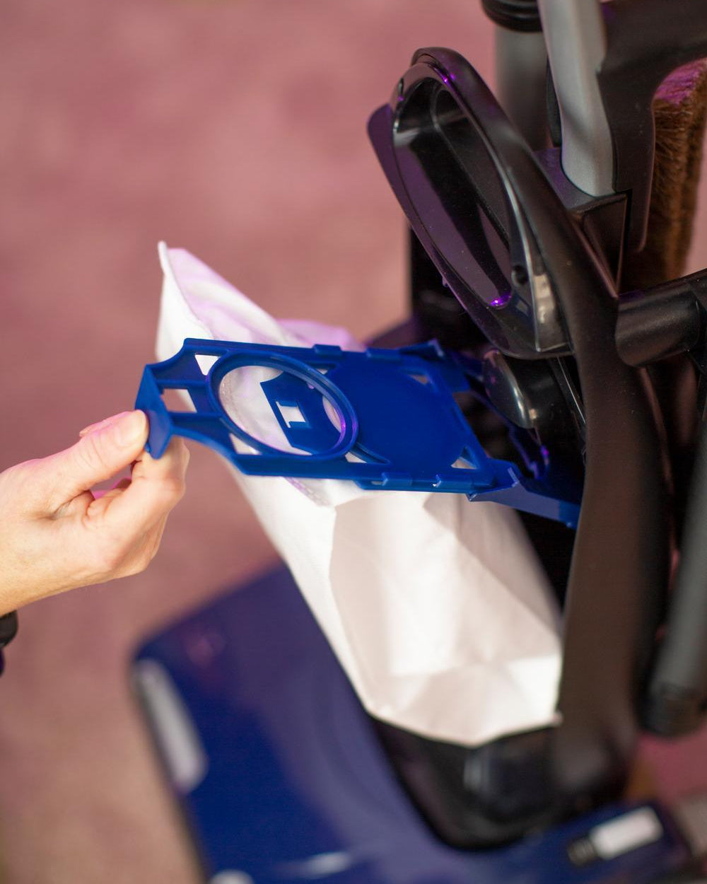 Person installing a blue plastic bag docking component onto a vacuum cleaner.