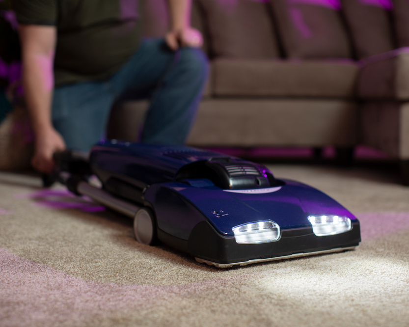Person vacuuming with a vacuum cleaner. Vacuum is laying flat on the carpet while still being operational.