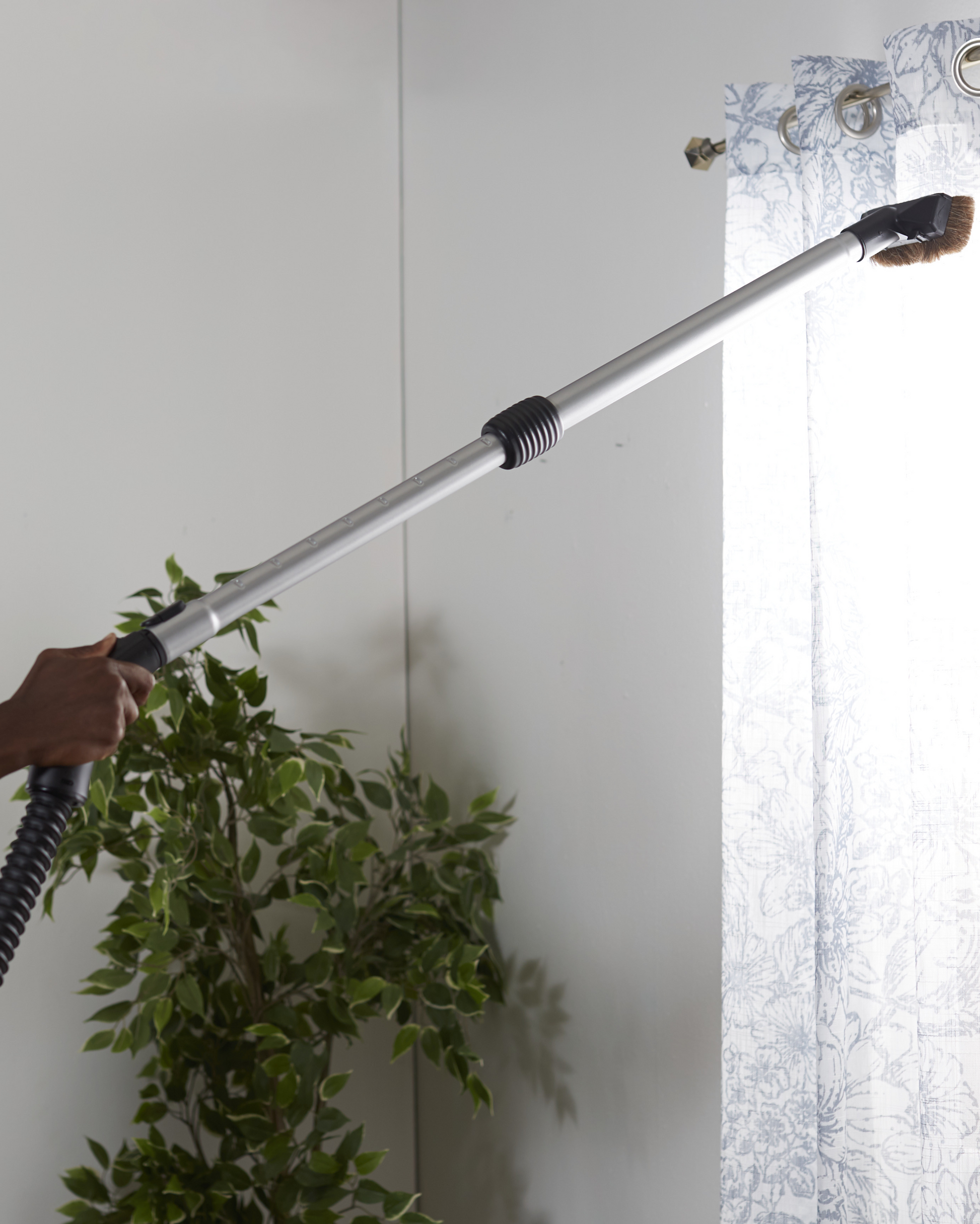 Person using a Riccar R40P vacuum hose and wand to clean a window.